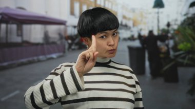 Hayır diyen bir kadın, hareketli bir şehir caddesinde, çizgili bir kazak giymiş, açık hava kentsel havasını kendine güvenen bir ifadeyle yakalıyor..