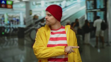 Havaalanı terminalinde sarı bir yağmurluk ve kırmızı bir bere takmış, kapalı bir alanda hareketli hareketler yapan genç İspanyol bir adam..