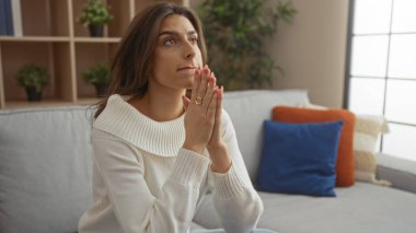 Sıcak bir oturma odasında, minderlerle ve sıcak dekorlarla çevrili düşünceli bir ifadeyle, huzurlu ve huzurlu bir atmosfer yaratan kapalı bir odada dua eden bir kadın..