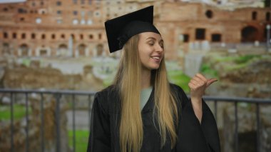 Mezuniyet elbisesiyle tarihi Roma harabelerinin arka planına bakan bir kadın..