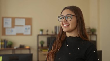 Raflar ve bitkilerle çevrili, modern ofiste gülümseyen genç bir kadın, sıradan bir iş ortamı öneriyor..