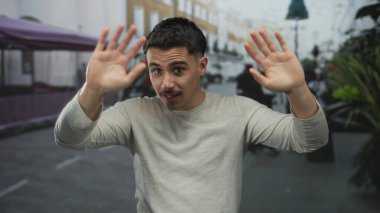 Genç İspanyol asıllı bir adam şehir sokaklarında neşeli hareketler yapıyor, çevresini çevreleyen hareketli şehir hayatı, neşeli bir ortamda neşe ve doğallığı ifade ediyor..