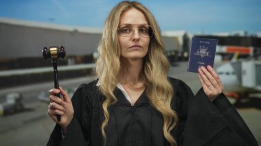 Kadın yargıç elinde Avustralya pasaportu ve tokmağı ile havaalanı terminalinde duruyor..