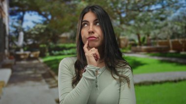 Yeşil parkın dışındaki genç İspanyol kadın, parmakları çenesinde düşünceli ve gür manzarayla çevrili, huzurlu ve düşünceli bir anı işaret ediyor..