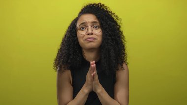 Genç İspanyol kadın, sarı bir duvarın üzerinden stüdyoda parmaklarını ovuşturarak endişeli bir bakış atar; çaresizce yardım için yalvarır..