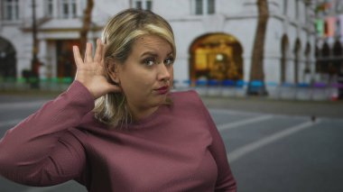 Kadın, beyaz bir binanın önündeki kalabalık bir şehir sokağında sarı saçlarını tarıyor..