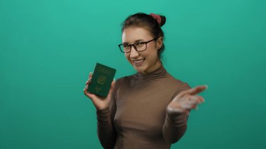 Güney Kore pasaportu taşıyan genç bir kadın, izole edilmiş yeşil bir arka plan duvarına karşı güvenle gülümsüyor, kimlik ve vize seyahat konsepti sergiliyor..