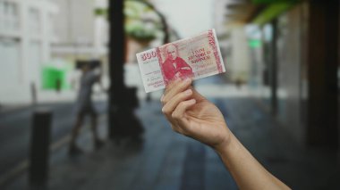 Bir şehir caddesinde İzlanda Krona banknotunu elinde tutan bir erkek şehir ortamında İzlanda parası sergiliyor..