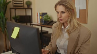 Ofiste çalışan kadın, arka planda bitki ve kitaplık bulunan bilgisayar masası yakınlarındaki gürültü nedeniyle kulaklarını kapatıyor.