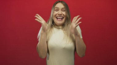 Sarı saçlı, neşeli tavırlı, izole edilmiş kırmızı arka planda heyecanını ifade eden bir kadın stüdyo ortamında canlı duygular ve pozitif enerji sergiliyor..