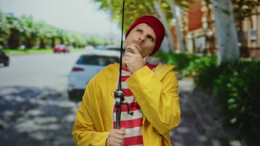 Sarı yağmurluklu İspanyol adam, şehir caddesinde nazikçe olta tutuyor, modern yaşam ve geleneksel aktivitenin karışımını somutlaştırıyor..