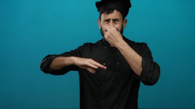 Siyah üniformalı İspanyol aşçı burnu kötü kokuya tepki veriyor. Mutfak ortamındaki iğrenme ifadelerini vurguluyor..