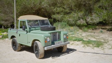 Kamptaki eski askeri aracın bulanık görüntüsü. Odaklanamayan yeşil ve kahverengi arka plan özellikleri vurguluyor..