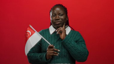 İzole edilmiş kırmızı arka planda Singapur bayrağı tutan bir kadın. Kendine güvenen ve gururlu görünen yeşil kazak giyen bir kadın..