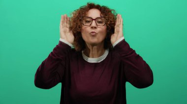 Gülümseyen ve neşeli bir şekilde yüzünü kapatan bir kadın, canlı yeşil bir arka plana karşı mutluluğu gözler önüne seriyor, anlamlı neşesini ve enerjisini vurguluyor..