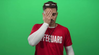 El kaplamalı genç İspanyol cankurtaran izole edilmiş yeşil arka plan duvarından endişeli görünüyor..