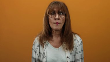 Turuncu arka planda gözlük takan, ekose gömlek giyen ve neşeli bir tavır sergileyen bir kadın..