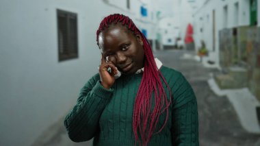 Kırmızı örgülü yeşil kazaklı bir kadın şehir arka planında duruyor ve şehirde duygularını gösteriyor.