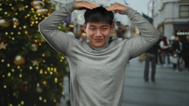 Gri tişörtlü, enerjik bir şekilde gülümseyen genç adam, neşeli şehir sokaklarında bayram kutlamaları için süslenmiş..