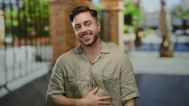 Sakallı genç adam, günlük tişörtler giymiş, şehir dışında arka planda yakalanmış, mutluluk ve rahatlama yayıyor..