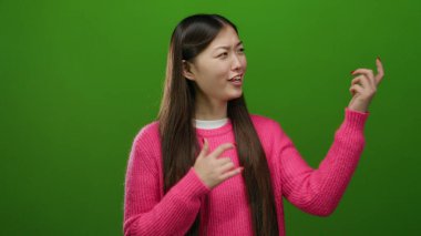 Gitar çalan kadın, canlı yeşil arka plana karşı pembe süveter giyerek güven içinde poz veriyor ve neşe ve yaratıcılığı yakalıyor.