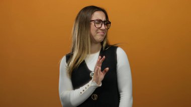 Gözlüklü bir kadın, portakal rengi bir arka plana karşı reddedilme hareketi gösteriyor. Ayrı bir ortamda, kaldırılmış bir elden ve hoşnutsuzluktan hoşnutsuzluğunu dile getiriyor..