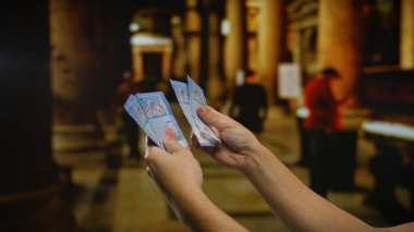 Bir kilisenin içinde Malezya sirkesi banknotları tutan bir adam, kapalı bir mekanda finans ve maneviyat arasındaki zıtlığı vurguluyor..