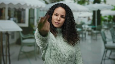 İspanyol kadın restoranın terasında el kol hareketleri yapıyor. Açık havada hayal kırıklığını dile getiriyor. Orta parmakları havada, duygusal bir anı yakalıyor..
