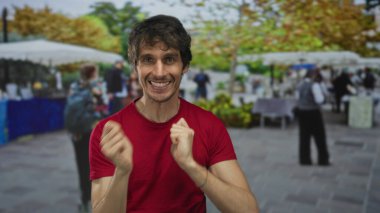 Kırmızı tişörtlü adam gülümsüyor ve yumruklarını sıkmış bir şekilde cadde pazarları arasında boks yapıyor; heyecan.