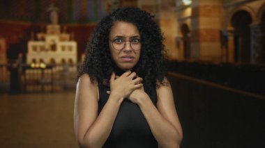 Yuvarlak gözlükler takan ve boğazını iki eliyle bir binanın içinde tutan genç İspanyol kadın. Korku..