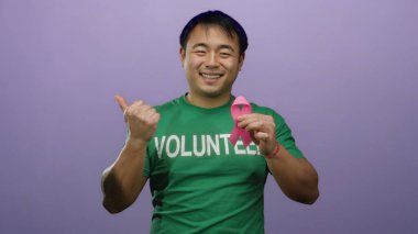 Mor arka planda pembe kurdele tutan Asyalı gönüllü gönüllü göğüs kanseri farkındalığını destekliyor..