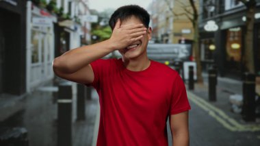 Kırmızı gömlekli genç adam şehir caddesinde bir şehir manzarasını neşe içinde resmediyor..