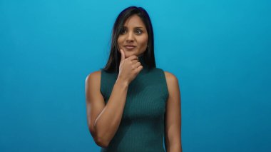 Işıl ışıl mavi bir zemin üzerinde düşünen bir kadın, düşünceli bir yüz ifadesiyle izole bir çerçeveye çekilmiş, İspanyol kökenli ve genç cazibesini vurguluyor.