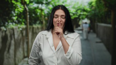 Bir kadın şehir caddesinde dışarıda dikilirken sessiz hareketler yapıyor, sakin ve huzurlu bir atmosferi somutlaştırıyor gün ışığında kentsel çevrede..