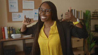 Profesyonel atmosferi olan bir ofis ortamında gülümseyen bir kadın, gözlüklü ve uzun saçlı, grafikler ve bitkilerle çevrili genç bir kadın..