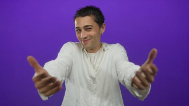 İzole edilmiş mor arka plana karşı el kol hareketi yapan genç bir İspanyol, stüdyo ortamında beyaz gömlek ve küpeler giyiyor.