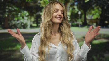 Güneşli bir park ortamında neşeli bir şekilde gülümseyen kadın, yemyeşil ağaçlarla çevrili, huzurlu bir açık havada mutluluk ve sükunet yayıyor..