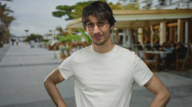 Lokanta terasında elleri kalçasında oturan, dışarı bakan, yaya geçidine bakan, kendine güveni olan adam..