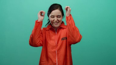 Turuncu hapishane tulumu giyen kadın canlı yeşil bir arkaplan karşısında neşeli bir şekilde dans ediyor, esmer saçı ve rahat tavırlarıyla neşe ve özgürlüğü ifade ediyor..