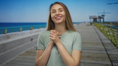 Genç bir kadın açık mavi suyla güneşli bir gezinti güvertesinde gülümsüyor, günlük giysiler giyiyor ve sakin açık havanın tadını çıkarıyor..