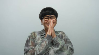 İzole edilmiş beyaz bir arkaplan üzerinde neşeli bir ifadeyle alkışlayan, çiçekli bir gömlek ve gözlük takan, mutluluk, coşku ve pozitif enerjiyi somutlaştıran bir kadın..