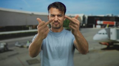 Arka planda bulanık uçaklarla havaalanında kaba jestler yapan Latin asıllı genç bir adam, açık hava seyahatlerinde hayal kırıklığı ve meydan okuma yaşıyor..