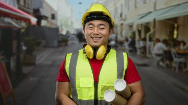 Güvenlik teçhizatı takan gülümseyen adam arka planda kafeleri olan bir şehir sokağının planlarını tutuyor..