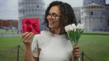 Çiçeklerden ve hediye kutusundan hoşlanan bir kadın açık hava kulesinin önünde bekliyor..