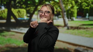 Gözlüklü kadın, parkın arka tarafını gösteren parmaklarıyla gülümsüyor..