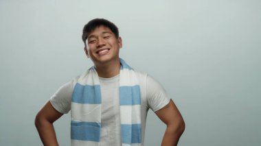 İzole edilmiş beyaz bir arka plana güvenle gülümseyen genç adam çizgili atkı ve beyaz gömlek giyiyor, neşeli ve pozitif bir tavır sergiliyor..