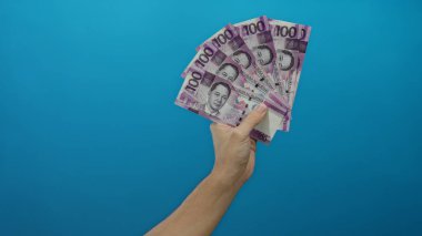 Beyaz adamın, Filipin pesolarını mavi bir duvara dayayıp, canlı ve izole bir ortamda servetini ve para birimini sergilemesi, finansal işlemleri vurgulaması,.