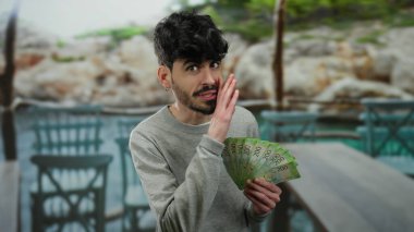 Elinde Rus rublesi tutan bir adam açık terasta restoran dekoruyla fısıldıyor, oyuncu ve yakışıklı görünüyor, elinde para ile sokak atmosferini yakalıyor..