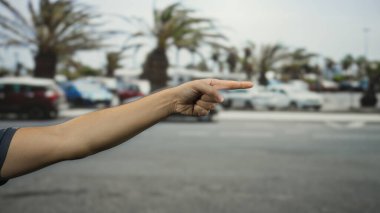 Güneşli bir günde dinamik bir şehir manzarası yakalayan, palmiye ağaçlarının ve park edilmiş arabaların bulanık arka planına sahip bir şehir caddesini gösteren bir adamın eli..