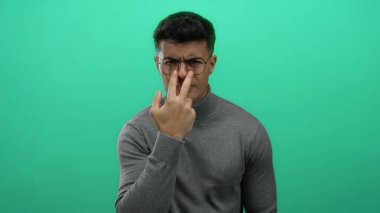 Genç adam canlı yeşil bir arka planda, gözlükleriyle güven içinde el kol hareketi yaparak, izole edilmiş, modern ve şık bir portre çiziyor..